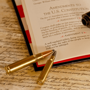 The image shows two gold bullets resting on a book that's opened to a page showing the first three amendments of the U.S. Constitution.