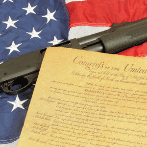 The image shows the Bill of Rights and a shotgun laying on top of the American flag.