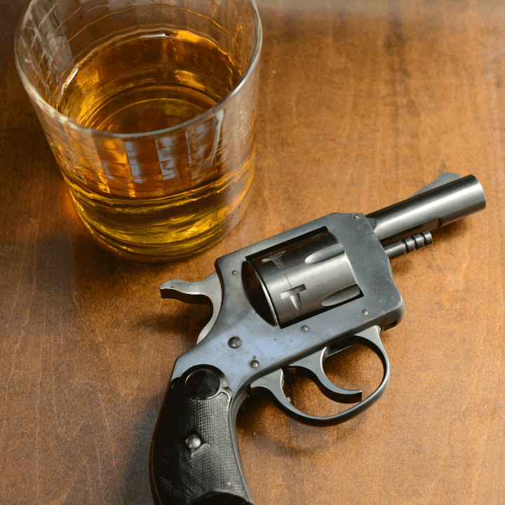 The image shows a gun laying on a table next to an alcoholic beverage.