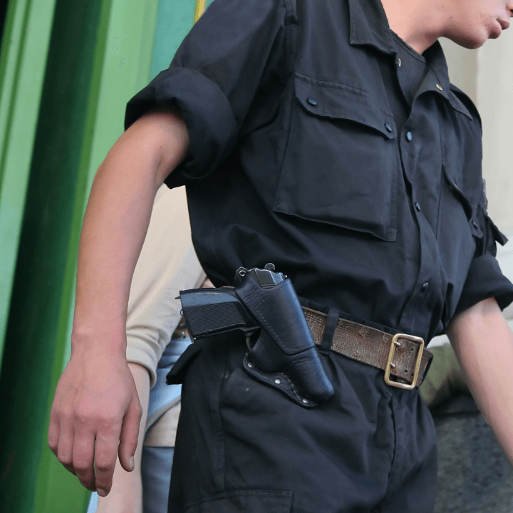 The image shows a man wearing all black carrying a handgun in a holster on his waist.
