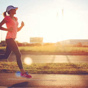 A woman running on a sidewalk wearing athletic gear and a hat