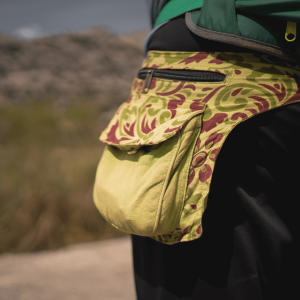 A close-up of a runner with a fanny pack on the side of their hip, grass and mountains in the background