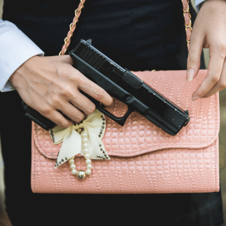 A closeup shot of a woman holding a handgun in front of a pink purse