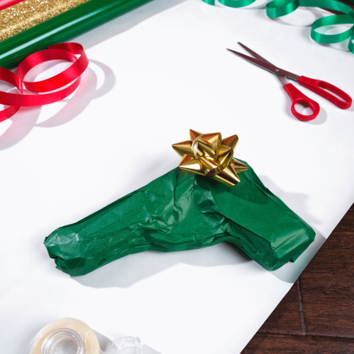 A gift-wrapped gun in green tissue paper and a gold bow