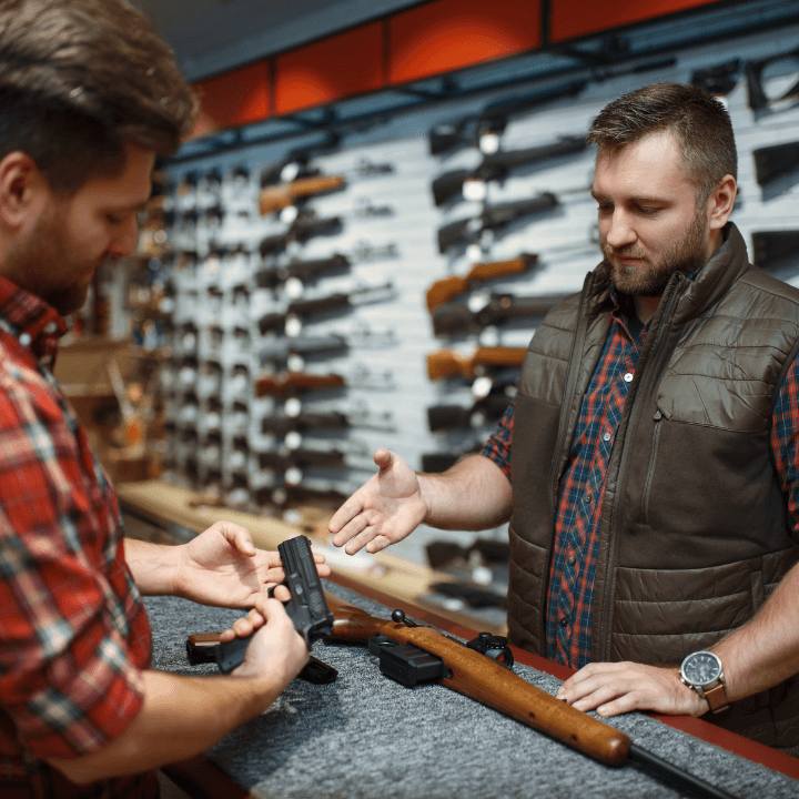 Two people at a gun store or gun shop looking at two guns on a table