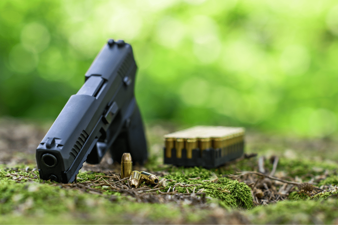 A handgun is lying with ammo on the ground in forest.