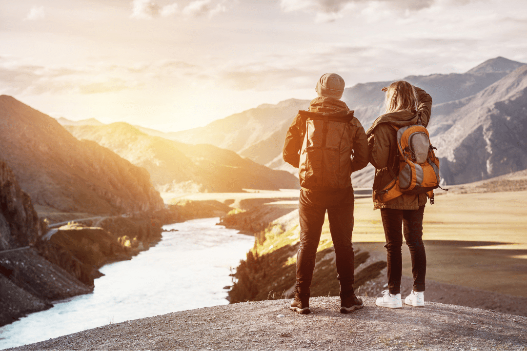 A couple is looking out into a sunset over a river and mountains.