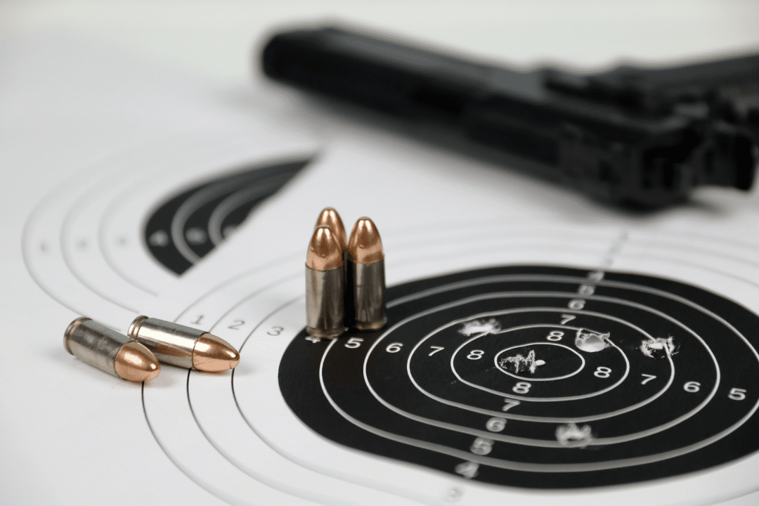 A handgun and ammo on top of a paper target with holes.